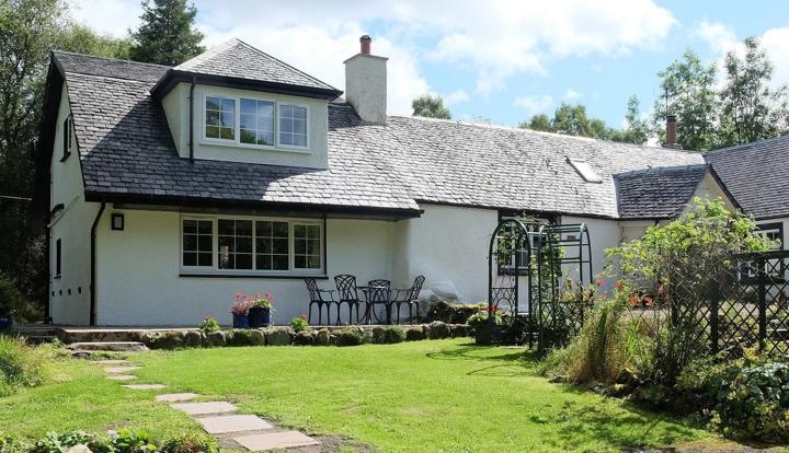Image of the front of the cottage showing grassy area, path & patio.